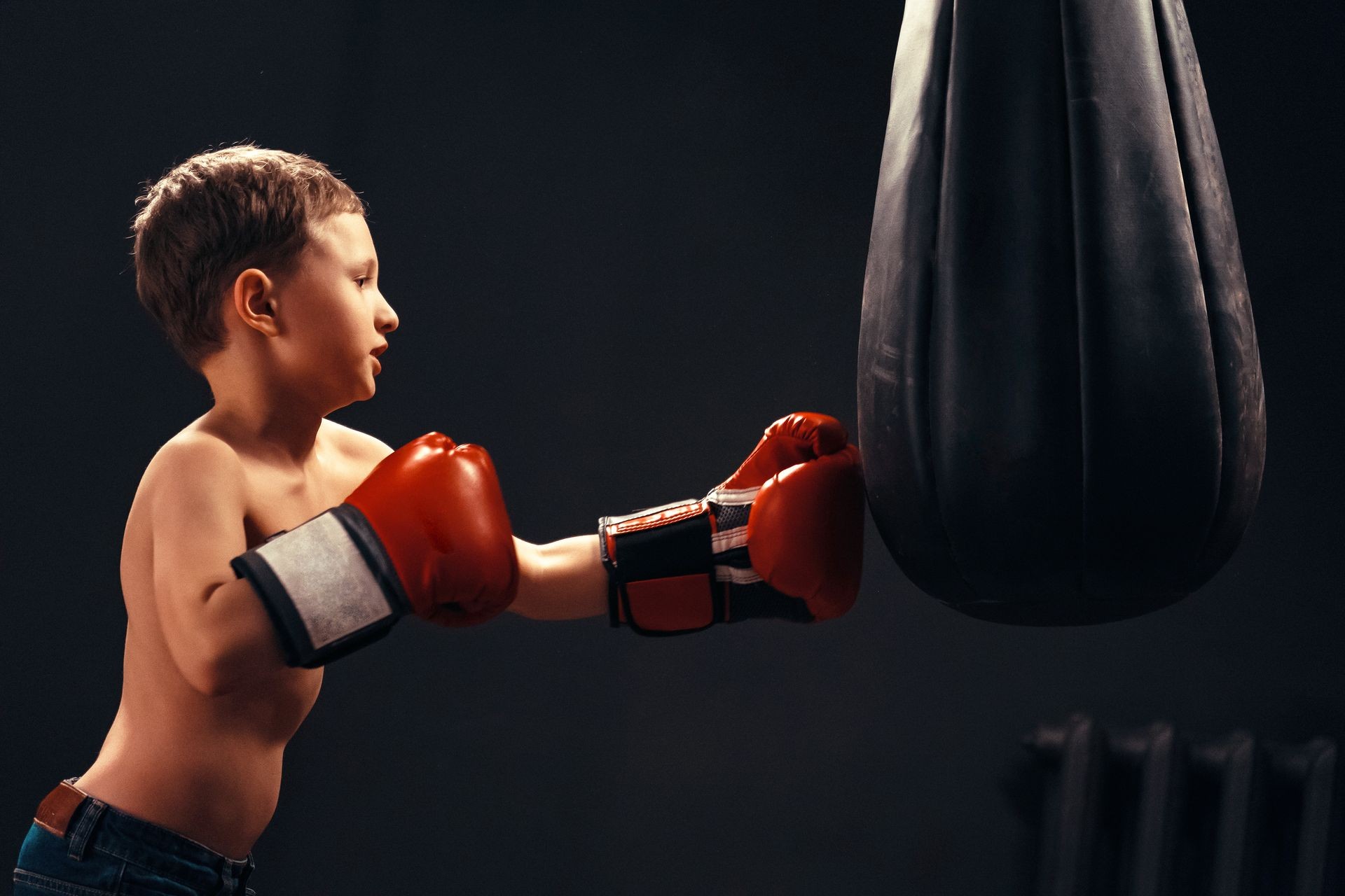 Boy hitting the punching bag on dark background. the aggression on sports training